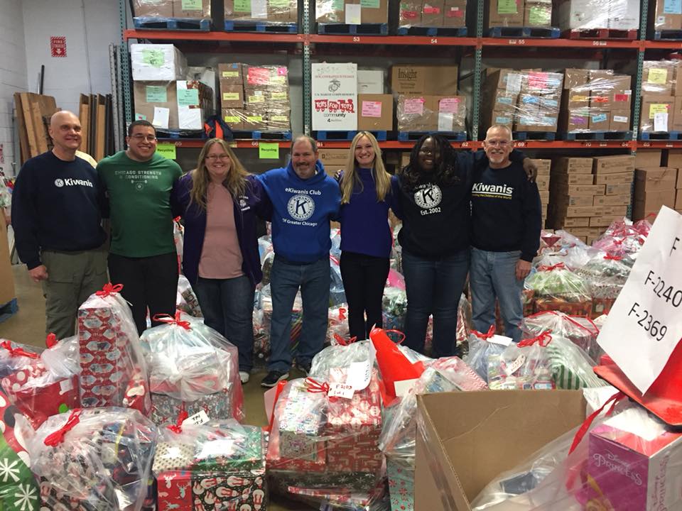 A group of 7 eKiwanis members standing behind large pile of holiday gifts